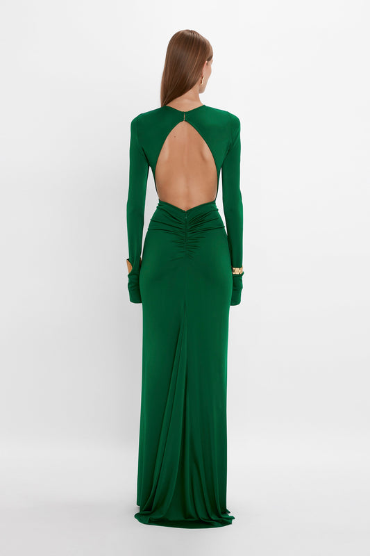 A person is standing with their back to the camera, wearing a Circle Detail Open Back Gown In Emerald by Victoria Beckham. The exposed back gown features a structured silhouette that complements their straight hair, which reaches just below their shoulders.