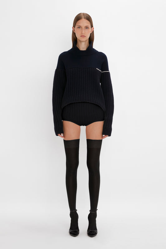 A woman in a black turtleneck sweater and Victoria Beckham Exclusive Over The Knee Socks in Black stands facing the camera on a white background.