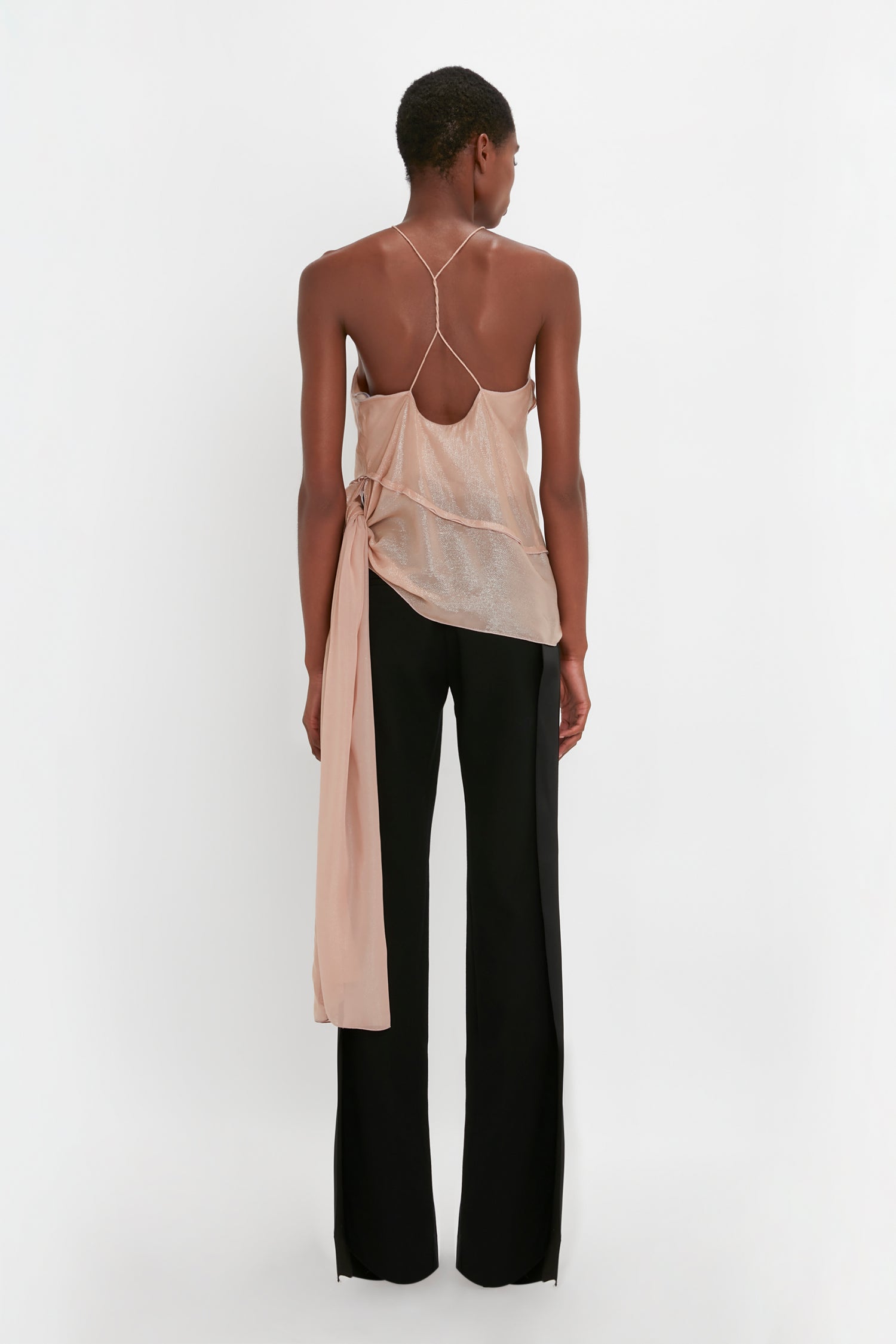 A person stands facing away, wearing a Victoria Beckham Flower Detail Cami Top In Rosewater. They pair it with black Satin Panel Straight Leg Trousers, against a plain white background.