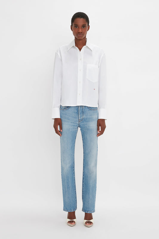A black woman wearing a Victoria Beckham Cropped Long Sleeve Shirt in White and blue jeans, standing against a plain white background.
