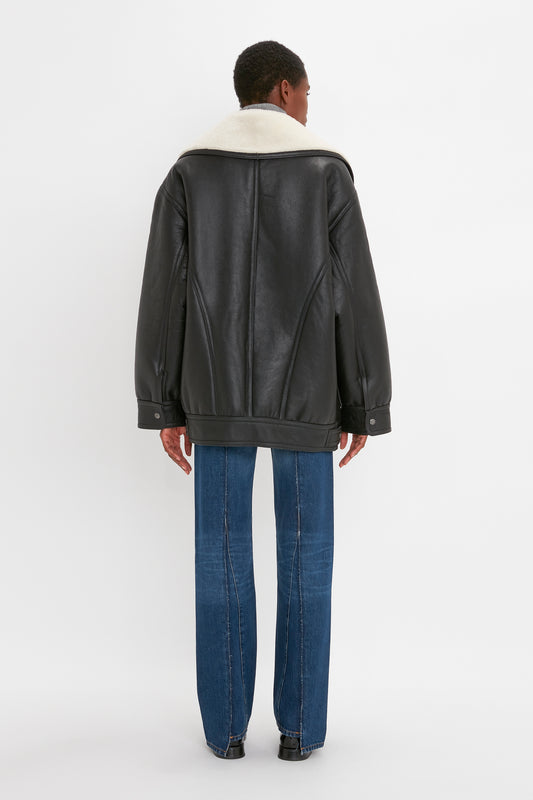 Person seen from the back wearing a Shearling Coat In Monochrome by Victoria Beckham with blue jeans, standing on a white background.