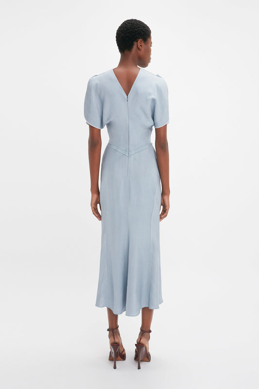 A woman seen from behind wearing a Victoria Beckham light blue Exclusive Gathered Waist Midi Dress In Pebble with brown high heels against a white background.