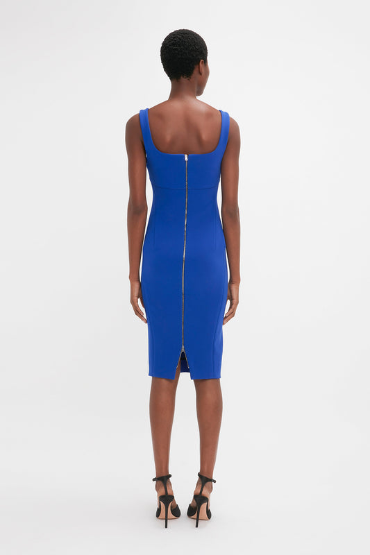 A person wearing a Sleeveless Fitted T-Shirt Dress In Palace Blue by Victoria Beckham with a back zipper and black high heels, standing with their back facing the camera.