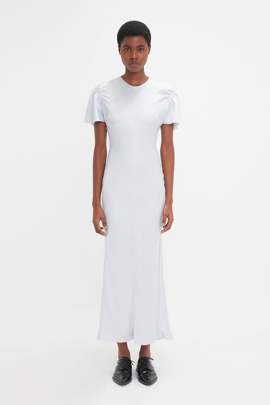Person stands against a white background wearing the Gathered Sleeve Midi Dress In Ice by Victoria Beckham, complete with delicate godet inserts and finished with black shoes.