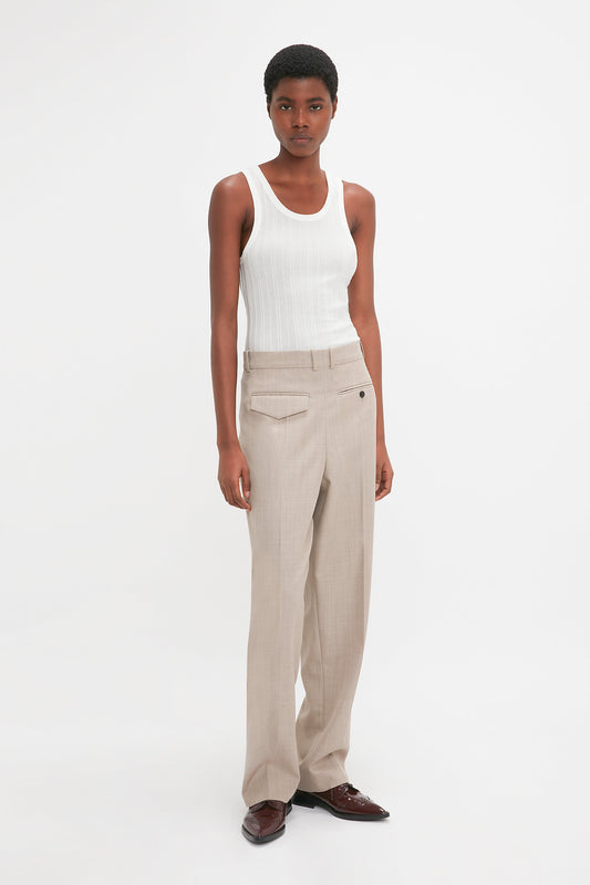 A person stands against a white background, wearing a Victoria Beckham Fine Knit Vertical Stripe Tank In White, beige trousers, and brown shoes.