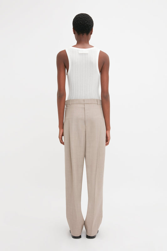 Person facing away from the camera, wearing a Victoria Beckham Fine Knit Vertical Stripe Tank In White and beige trousers, against a plain white background.