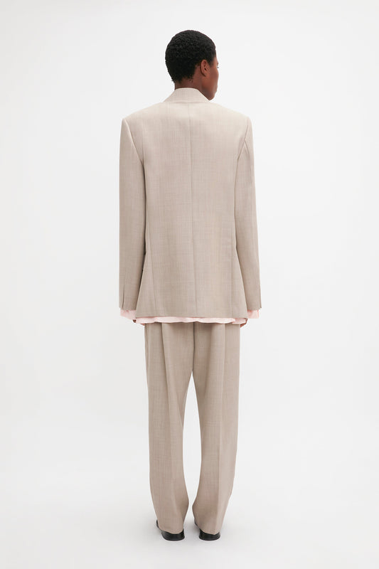 A person in a Darted Sleeve Tailored Jacket In Sesame by Victoria Beckham stands facing away from the camera against a white background.