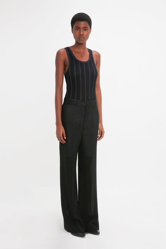 A person stands against a plain white background wearing a Victoria Beckham Fine Knit Vertical Stripe Tank In Black-Blue and black wide-leg pants, looking directly at the camera.