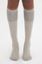 A person's legs from the knees down wearing Lunar Grey knee-high socks. The 100% cotton Victoria Beckham Superfine Rib Socks In Lunar Grey feature a ribbed texture with a smooth finish near the top, adding a touch of subtle elegance.