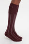 Dark red knee-high socks, made of 100% cotton, with white vertical stripes on a person's lower legs, set against a plain white background. This Burgundy and White design showcases the elegance and comfort of Superfine Rib Socks In Burgundy by Victoria Beckham.