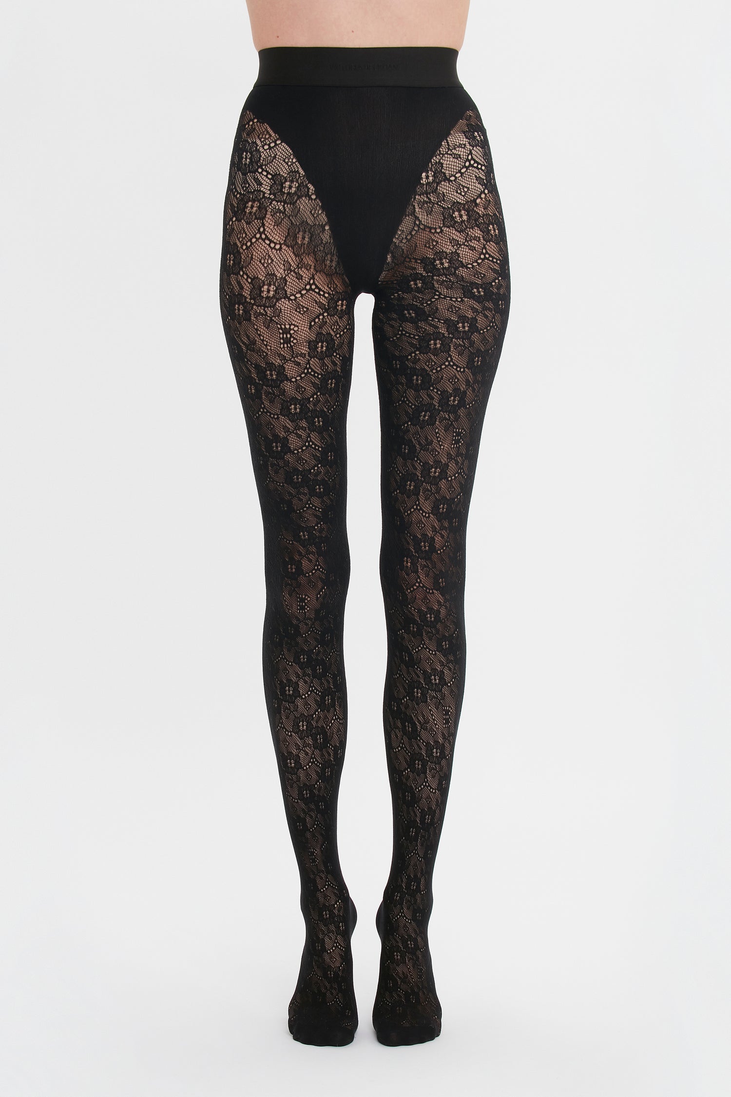 A person wearing ornate Victoria Beckham Exclusive VB Monogram Lace Tights in Black against a white background.