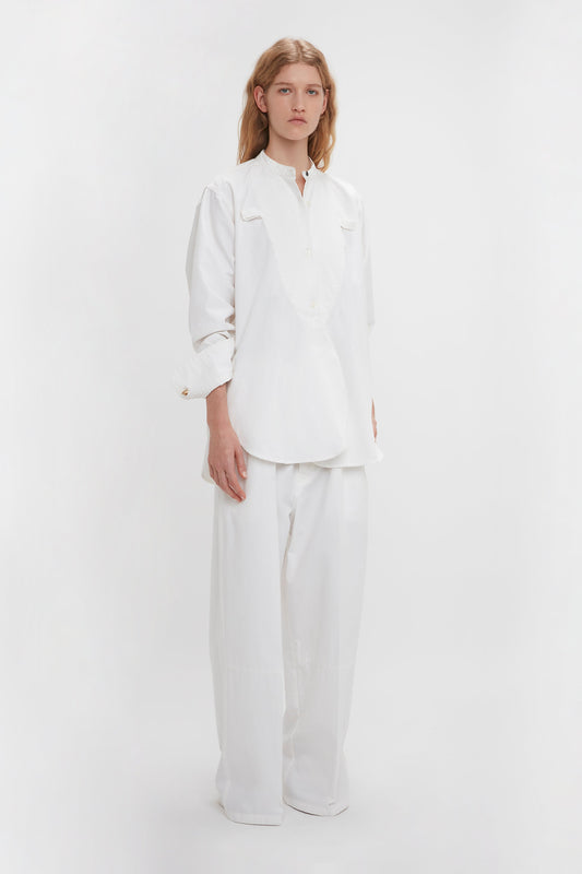 Person in a Bib-Front Tuxedo Shirt In Washed White by Victoria Beckham and wide-leg pants, standing against a plain white background.
