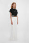 A person with long hair stands against a white background wearing a black 'Do As I Say, Not As I Do' Slogan T-Shirt In Black by Victoria Beckham and wide-leg white pants with a dark belt.