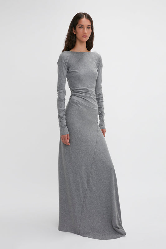 A woman stands in a grey, Long Sleeve Circle Neck Dress In Grey Marl by Victoria Beckham made from a super-soft cotton-jersey blend. She faces forward with her arms by her sides against a plain white background, embodying contemporary eveningwear elegance.
