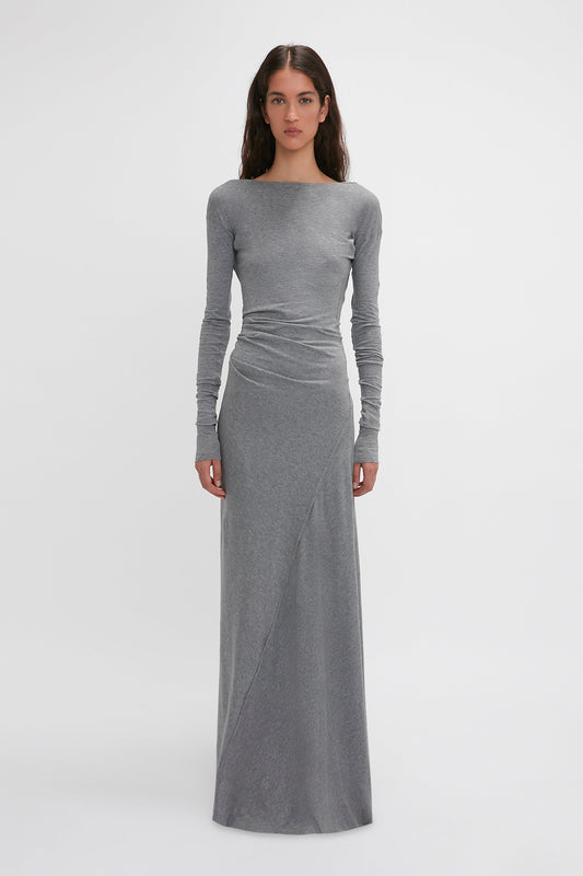 A woman with long dark hair is wearing a long-sleeved, fitted gray Long Sleeve Circle Neck Dress In Grey Marl by Victoria Beckham. She stands against a plain white background, facing forward.