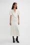 A woman stands wearing the Gathered V-Neck Midi Dress In Ivory by Victoria Beckham, paired with black heeled boots against a plain white background.