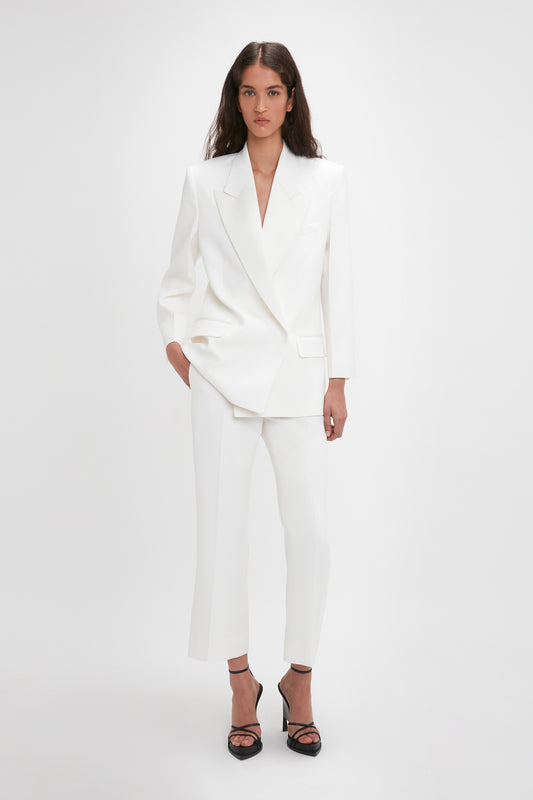 Person wearing a white tailored blazer and Victoria Beckham Exclusive Cropped Tuxedo Trouser In Ivory with black heeled sandals, standing against a plain white background.
