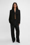 A woman in a sleek black suit with a Victoria Beckham Fold Detail Tailored Jacket featuring folded detail and straight leg trousers, standing against a plain white background.