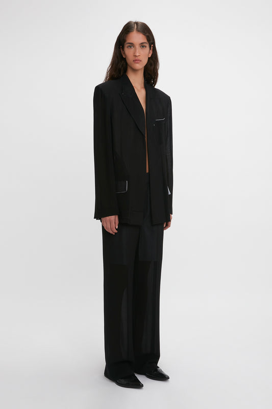 A woman stands facing forward, wearing a stylish Victoria Beckham Fold Detail Tailored Jacket in Black with matching straight leg trousers, set against a plain white background.