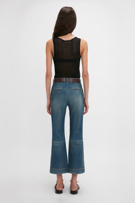 A person with long hair is standing with their back to the camera, wearing a black Lightweight Tank Top In Black by Victoria Beckham and blue flared jeans.
