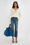 A woman stands against a plain backdrop, wearing a white long-sleeve top, blue jeans, and heeled sandals, holding a Victoria Beckham W11 Medium Tote Bag In Vibrant Blue.