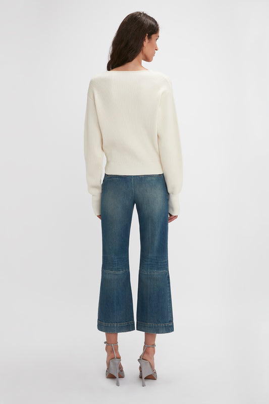 A woman viewed from behind wearing a cream sweater and Victoria Beckham's Cropped Kick Jean In Indigrey Wash, standing against a plain white background.