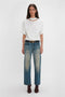 Person standing against a white background, wearing a white Victoria Beckham Bonded Jersey Tee In White with dropped shoulders and a relaxed cut, blue denim jeans, burgundy boots, and a black belt.