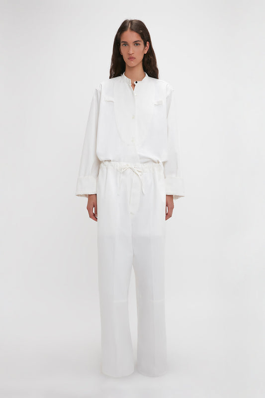 A young woman models a white long-sleeved blouse and cotton-canvas Victoria Beckham Drawstring Pyjama Trousers in Washed White with an adjustable drawstring waistband, standing against a plain light background.