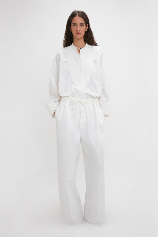 A woman in a white jumpsuit with an adjustable drawstring waistband stands against a plain background. 
    - A woman in Victoria Beckham Drawstring Pyjama Trouser In Washed White stands against a plain background.