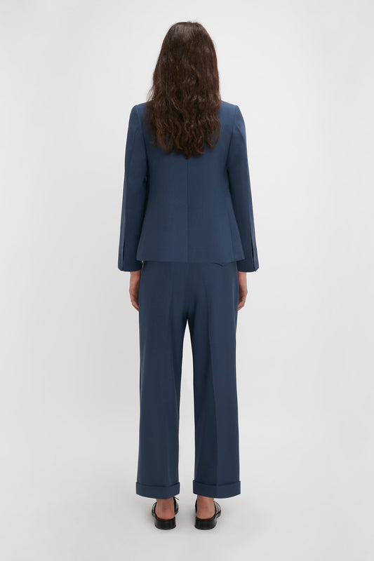 Rear view of a woman with long, wavy hair, wearing a Victoria Beckham Shrunken Double Breasted Jacket In Heritage Blue and black shoes, standing against a white background.