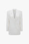 A white double-breasted wool-blend blazer with a deep V neckline, notched lapels, and structured shoulders. The Exclusive Double Breasted Tuxedo Jacket In Ivory by Victoria Beckham has two front flap pockets and a clean, minimalist design perfect for black-tie occasions.