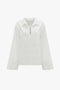 The Victoria Beckham Oversized Embroidered Tunic In Antique White is a vintage-inspired white long-sleeved blouse with a collar and a small front cut-out. Decorative stitching is present on the front, adding to its charm. Crafted from a linen-cotton blend, this relaxed-fit tunic offers both style and comfort.