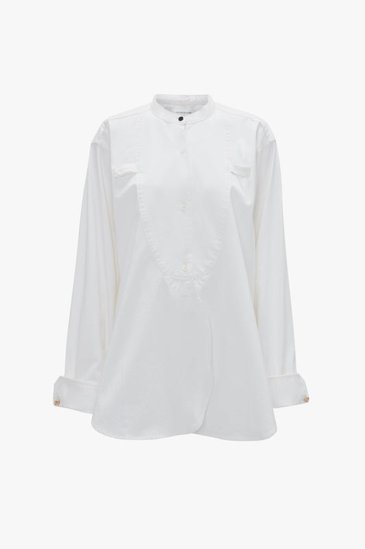 A white long-sleeve button-up shirt with a stand collar, curved front placket, and refined Bib-Front detailing. Crafted from 100% cotton for a relaxed fit, the Victoria Beckham Bib-Front Tuxedo Shirt In Washed White.