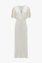 A sophisticated Victoria Beckham Gathered V-Neck Midi Dress In Ivory featuring a flattering V-neck, short puff sleeves, waist-defining pleat detail, and a twisted front accent for an elegant touch.