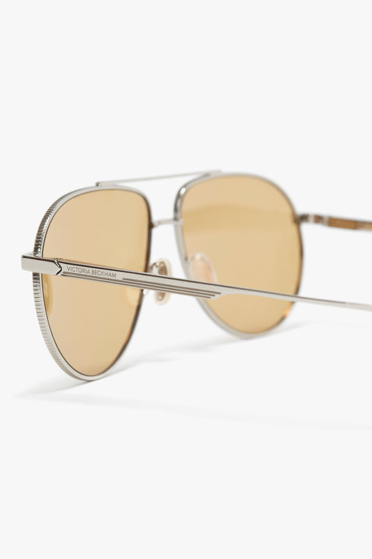 Pair of Victoria Beckham V Metal Pilot Sunglasses In Silver-Brown with brown lenses and thin metal frames, featuring adjustable nose pads, set against a white background.