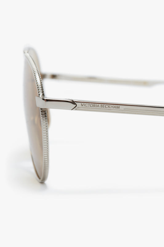 Close-up of the side arm of Victoria Beckham V Metal Pilot sunglasses showing the Victoria Beckham logo on a white background.