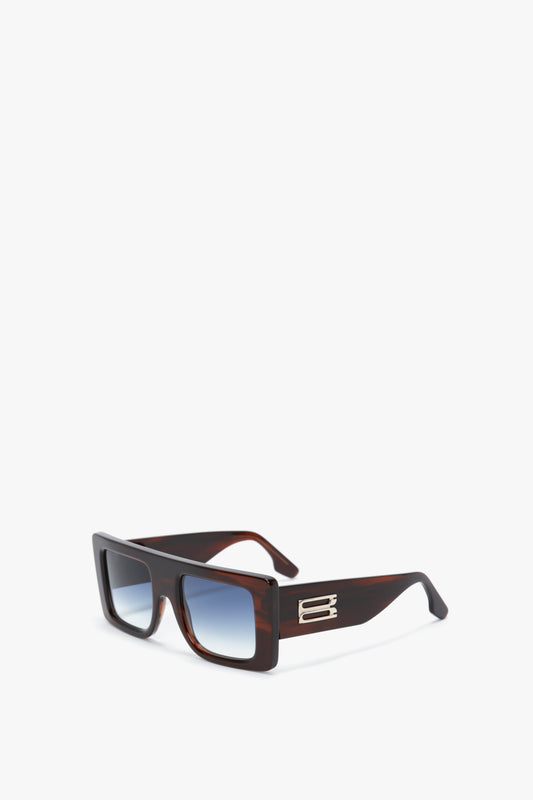 Rectangular, brown-framed sunglasses with blue gradient lenses and metallic detailing on the arms in a bold oversized frame, shown on a white background. The product is Oversized Frame Sunglasses In Brown Horn by Victoria Beckham.