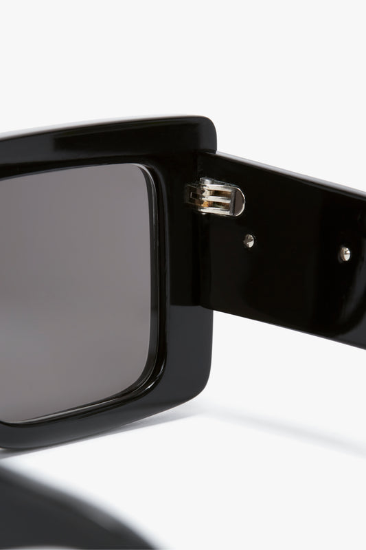 Close-up of the Oversized Frame Sunglasses In Black by Victoria Beckham on a pair of black oversized sunglasses with dark lenses, showcasing the connection between the frame and the temple, reminiscent of styles seen on the SS24 runway.