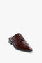 A single luxurious calfskin leather dress shoe, featuring decorative perforations and a pointy toe. The shoe has a closed lace-up design but is backless, resembling Victoria Beckham’s Flat Lace Up Mules In Bordeaux Leather.