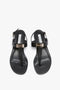 Top view of a pair of black Flat Chain Sandal In Black Leather with adjustable ankle straps, gold hardware detailing, and the brand label "Victoria Beckham" on the calfskin leather insole.