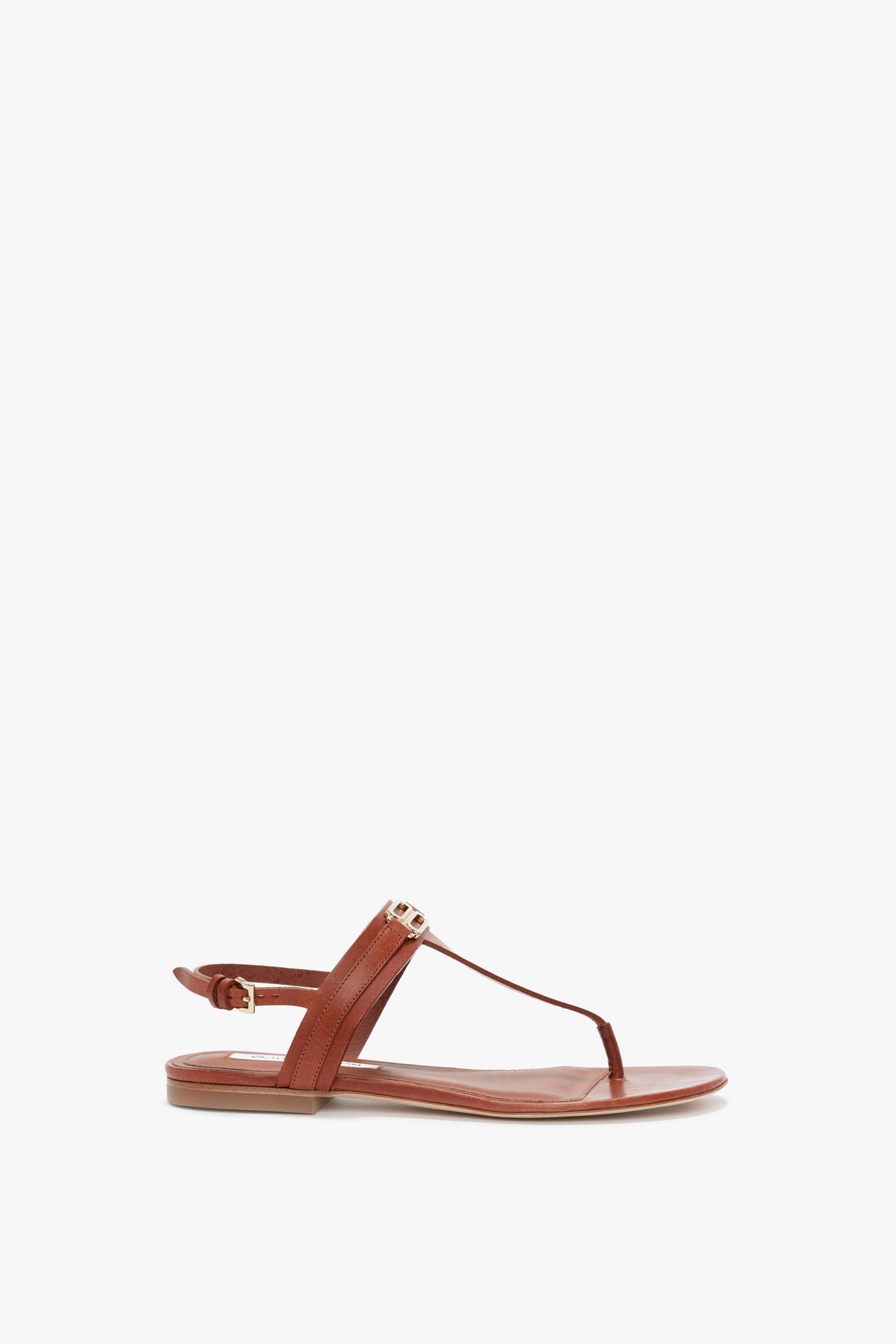 Victoria Beckham's Flat Chain Sandal In Tan Leather, adorned with a gold-tone chain, featuring a flat sole and adjustable ankle strap buckle, displayed against a white background.