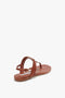 A single, brown Flat Chain Sandal In Tan Leather by Victoria Beckham with a thong design and an adjustable ankle strap, viewed from the rear and slightly to the left.