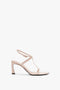 The Victoria Beckham Frame Detail Sandal In Nude Leather features a single nude-colored heeled design with an adjustable ankle strap, complemented by a thin strap and a V-shaped sculptural heel on a white background.