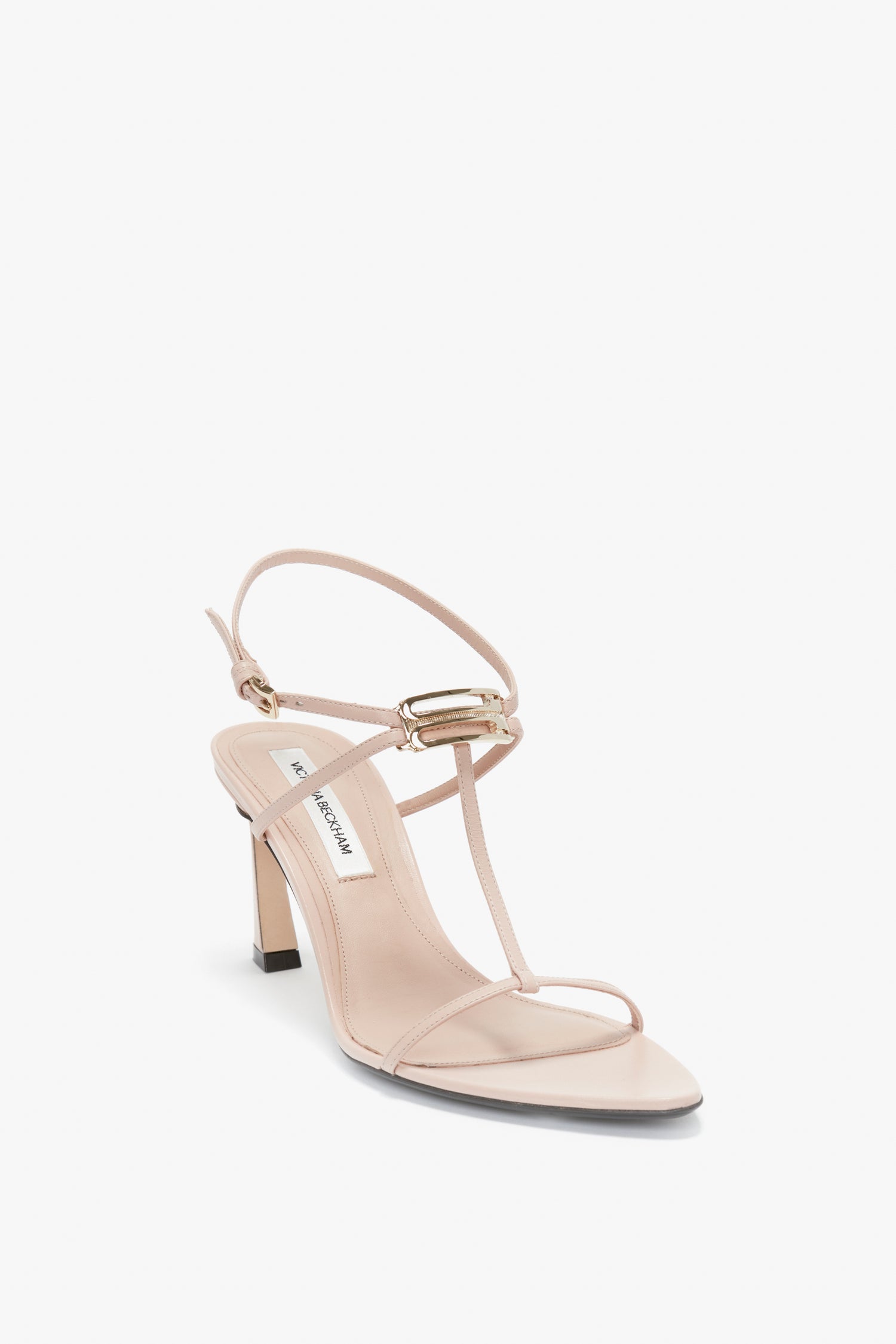 A single nude Frame Detail Sandal In Nude Leather by Victoria Beckham, featuring thin straps, a small buckle on the upper strap, an adjustable ankle strap, and a V-shaped sculptural heel on a white background.