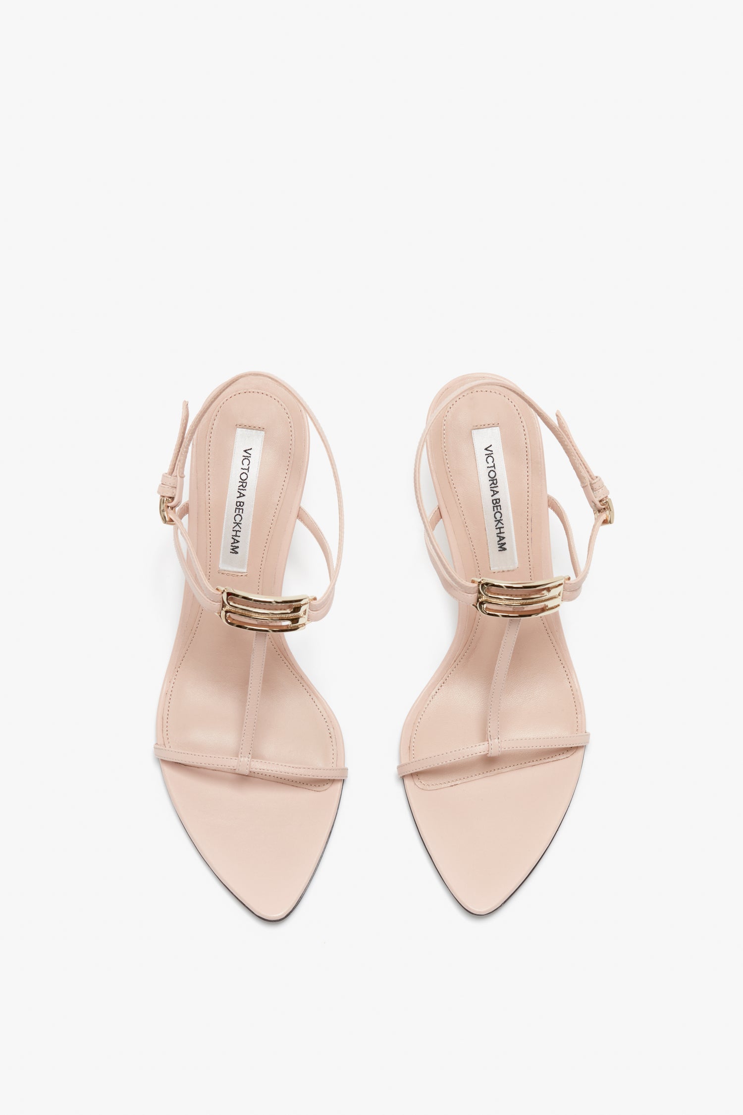 Victoria Beckham Frame Detail Sandal In Nude Leather with gold buckles, toe straps, and an adjustable ankle strap, featuring V-shaped sculptural heels viewed from above against a white background.