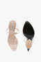 Top and bottom view of the Frame Detail Sandal In Nude Leather by Victoria Beckham, featuring a pair of strappy, high-heeled sandals in nude color. The insole showcases a metallic logo, while the left shoe’s black sole is pointed with product details. The V-shaped sculptural heel and adjustable ankle strap complete the elegant design.