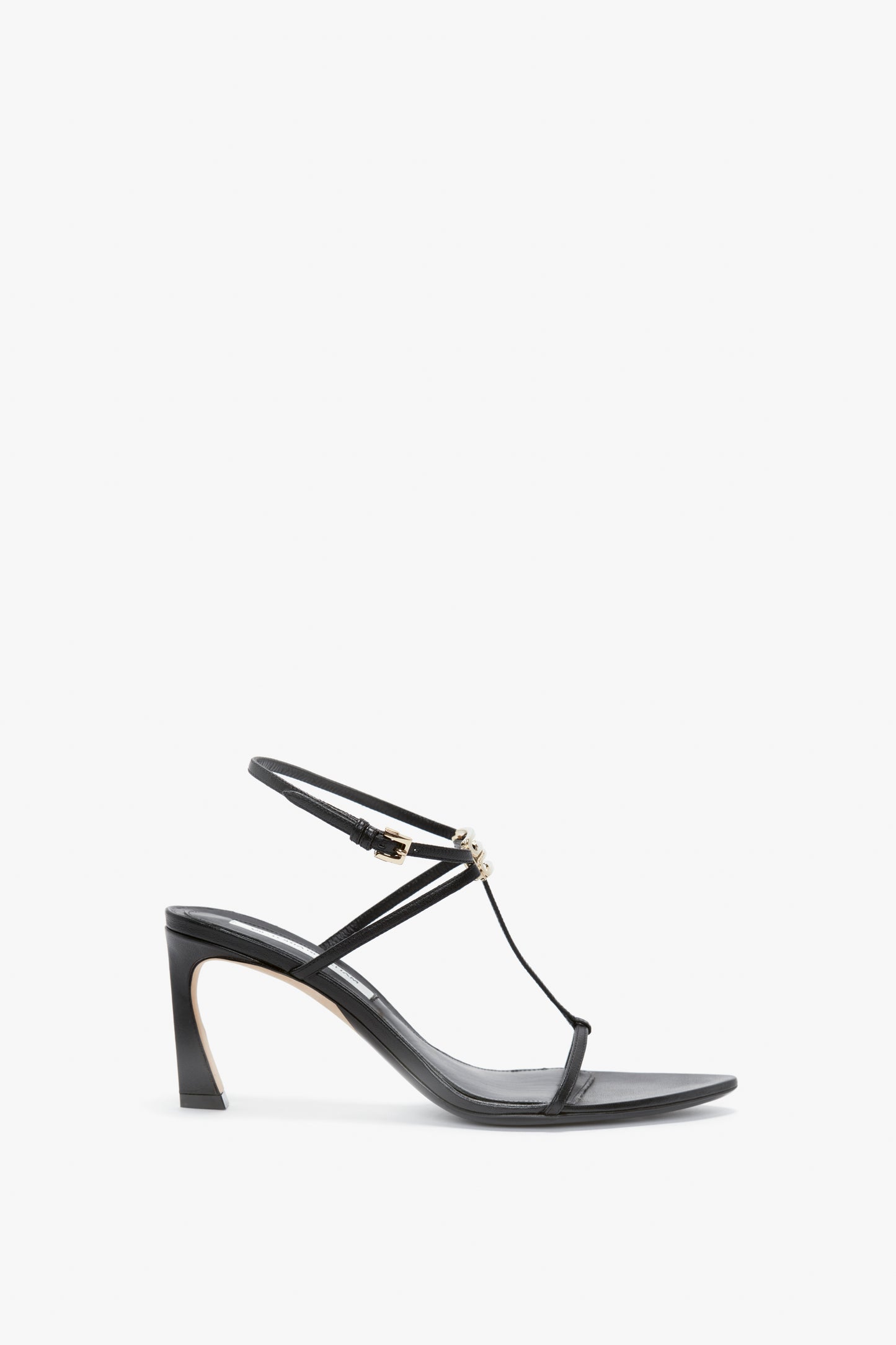 A Frame Detail Sandal In Black Leather by Victoria Beckham, featuring thin nappa leather straps, a minimalist design, and a small decorative bead on the front strap, with an adjustable ankle strap and set against a white background.