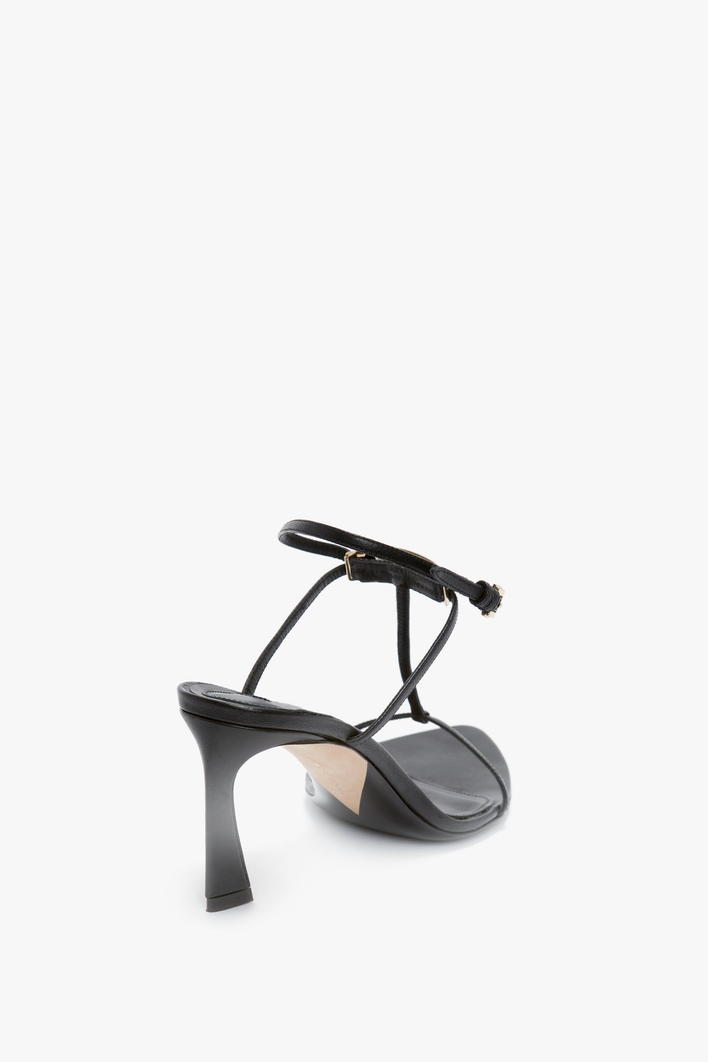 A Victoria Beckham Frame Detail Sandal In Black Leather with thin straps, a sculptural heel, and an adjustable ankle strap, viewed from the back and slightly to the side against a white background.
