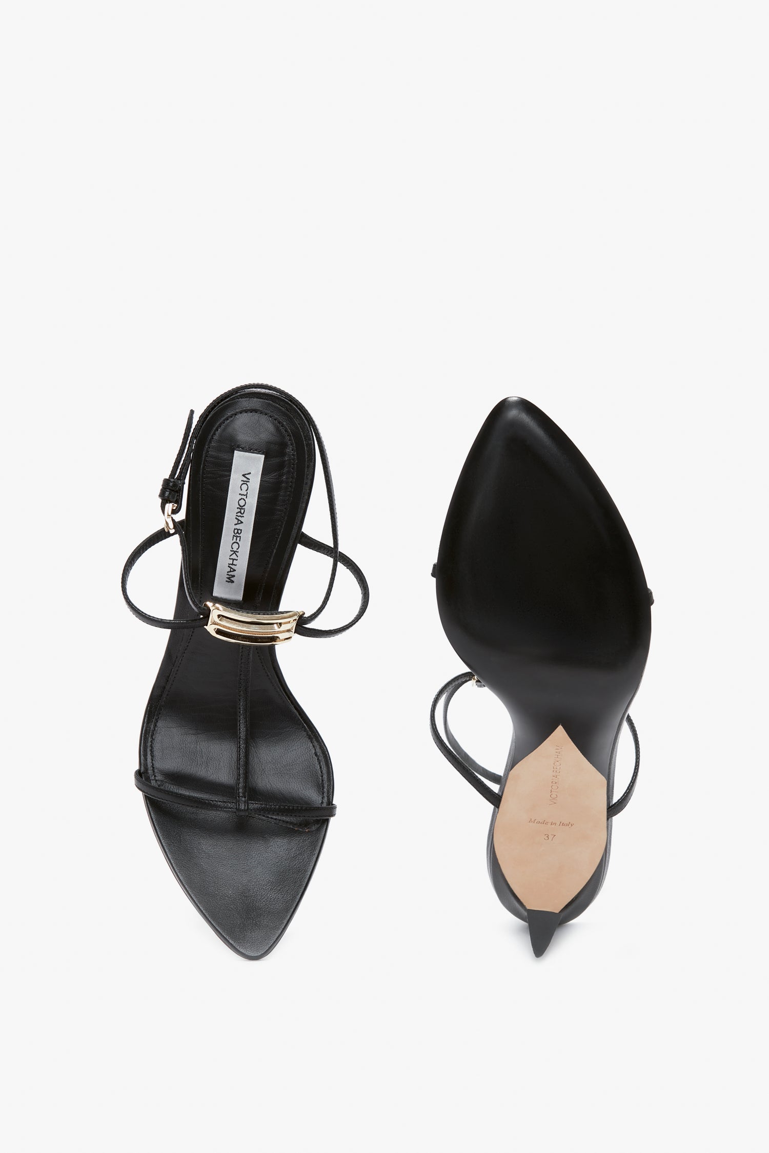 Top and bottom view of a pair of black high-heeled strappy sandals, featuring pointed toes and a gold buckle on the adjustable ankle strap. The shoes boast sculptural heels that add an artistic flair to the design. Introducing the **Frame Detail Sandal In Black Leather** by **Victoria Beckham**.