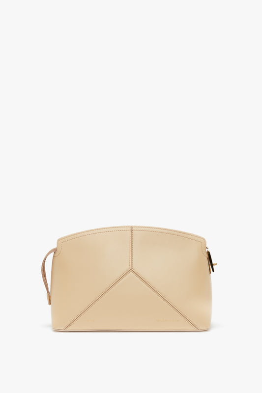 Beige leather handbag with a structured design and a wrist strap on the left side. The Victoria Clutch Bag In Sesame Leather by Victoria Beckham, Victoria’s favourite, has stitching details forming a geometric pattern on the front, resembling designs showcased in SS24 runway collections.